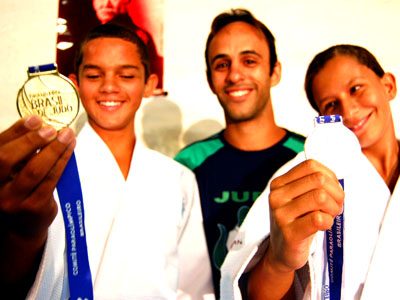 Nathan e Pâmela presentam suas medalhas conquistadas em maio junto com o instrutor Gleyson -