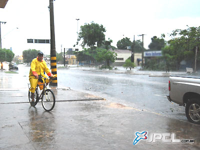 Ciclista trafega pela calçada, tentando se proteger melhor da chuva, na manhã de ontem -