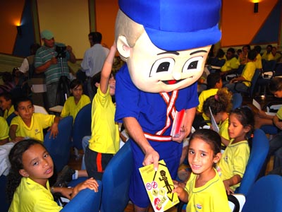 Crianças recebem caderneta de multas das mãos do mascote da campanha -