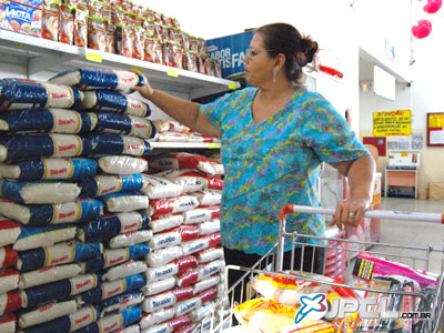 Dona de casa analisa preços de produtos, como feijão, arroz, na prateleira de um supermercado -