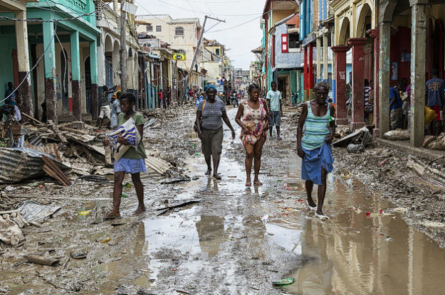 Mulheres caminham em rua alagada, com prédios destruídos, em cidade haitiana - Divulgação/ONU