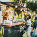 Multiethnic friends standing in queue and ordering takeaway dishes from man in apron working in food truck in summer in park