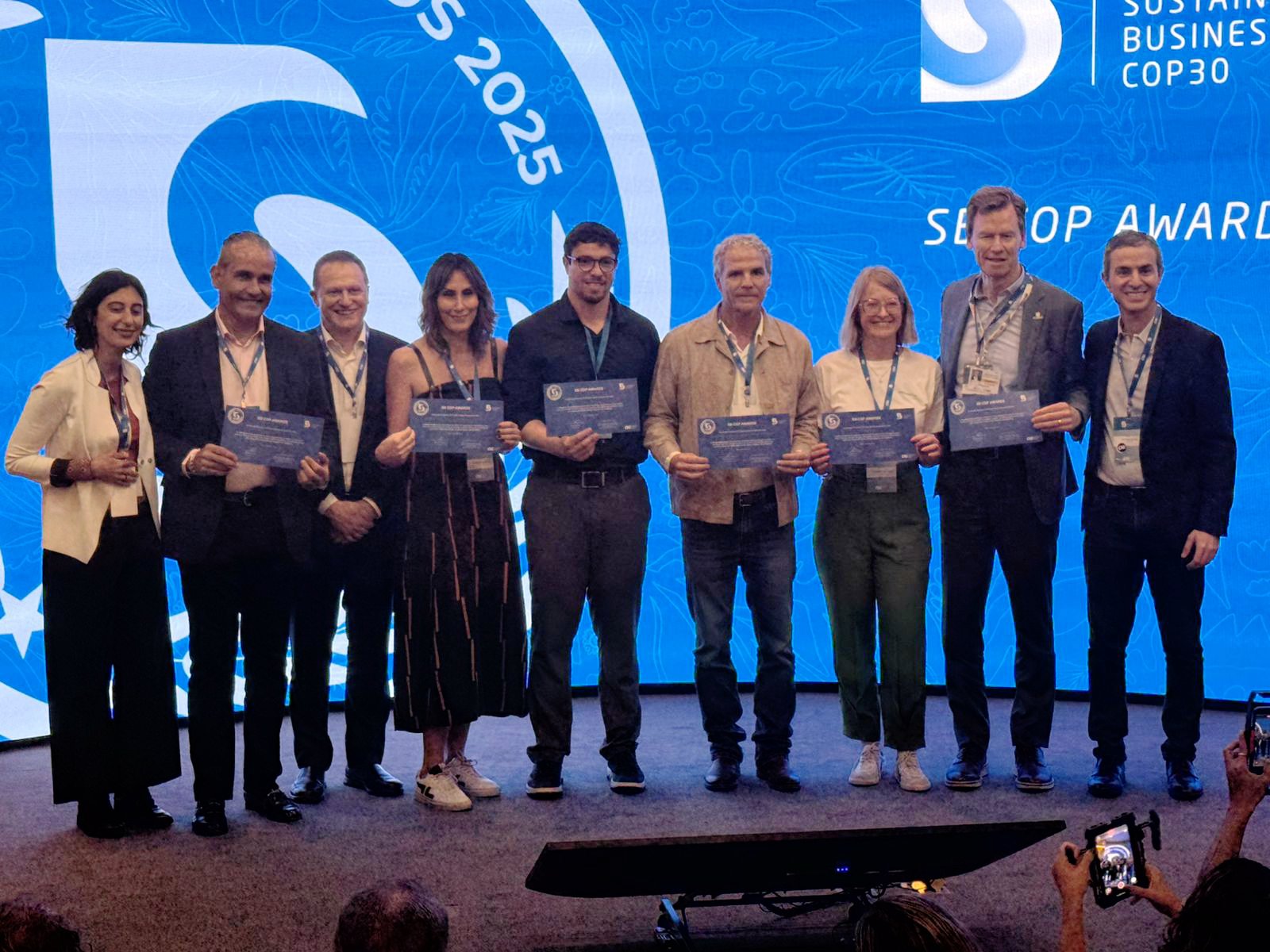 Representantes da JBS recebem premiação em palco na COP30, segurando troféu, com painel sobre economia de baixo carbono ao fundo.