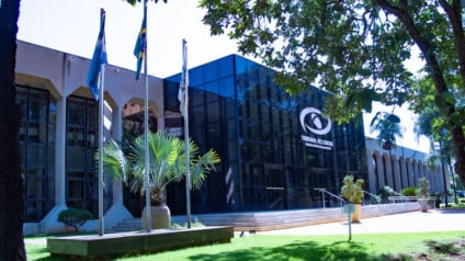 Fachada de prédio institucional com documentos oficiais e símbolos genéricos de gestão pública e controle externo ao fundo.