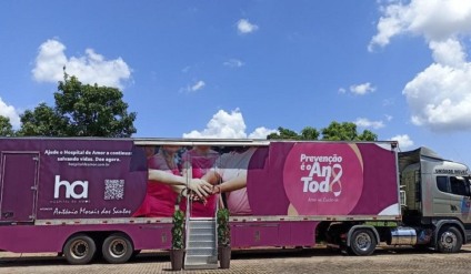 Carreta de unidade móvel de saúde estacionada em avenida de cidade pequena, com mulheres formando fila para atendimento pela manhã
