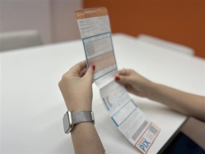 Pessoa usando celular com app de serviços e conta de energia sobre a mesa, cenário doméstico, sem logotipos